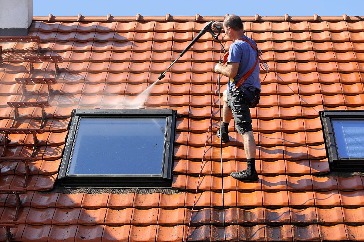 Arbeiter führt Dachreinigung mit Hochdruck auf Ziegeldach um Dachfenster durch – CleanTown24