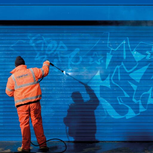 Arbeiter entfernt Graffiti von blauer Rollladenfläche mit Hochdruckreiniger – CleanTown24